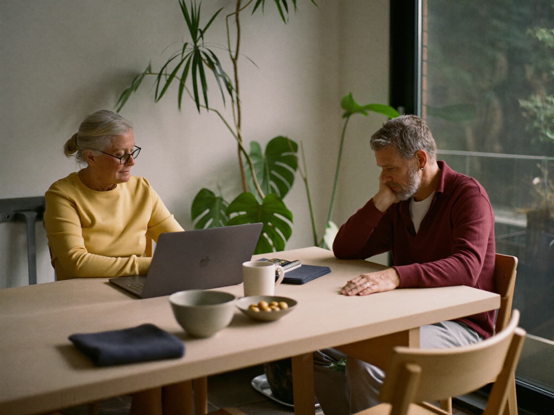 Twee mensen zitten aan de keukentafel en kijken samen naar een laptopscherm.