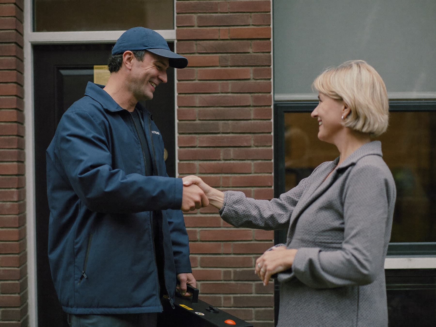 Technicus met gereedschapskoffer geeft een bewoner een hand bij de voordeur.
