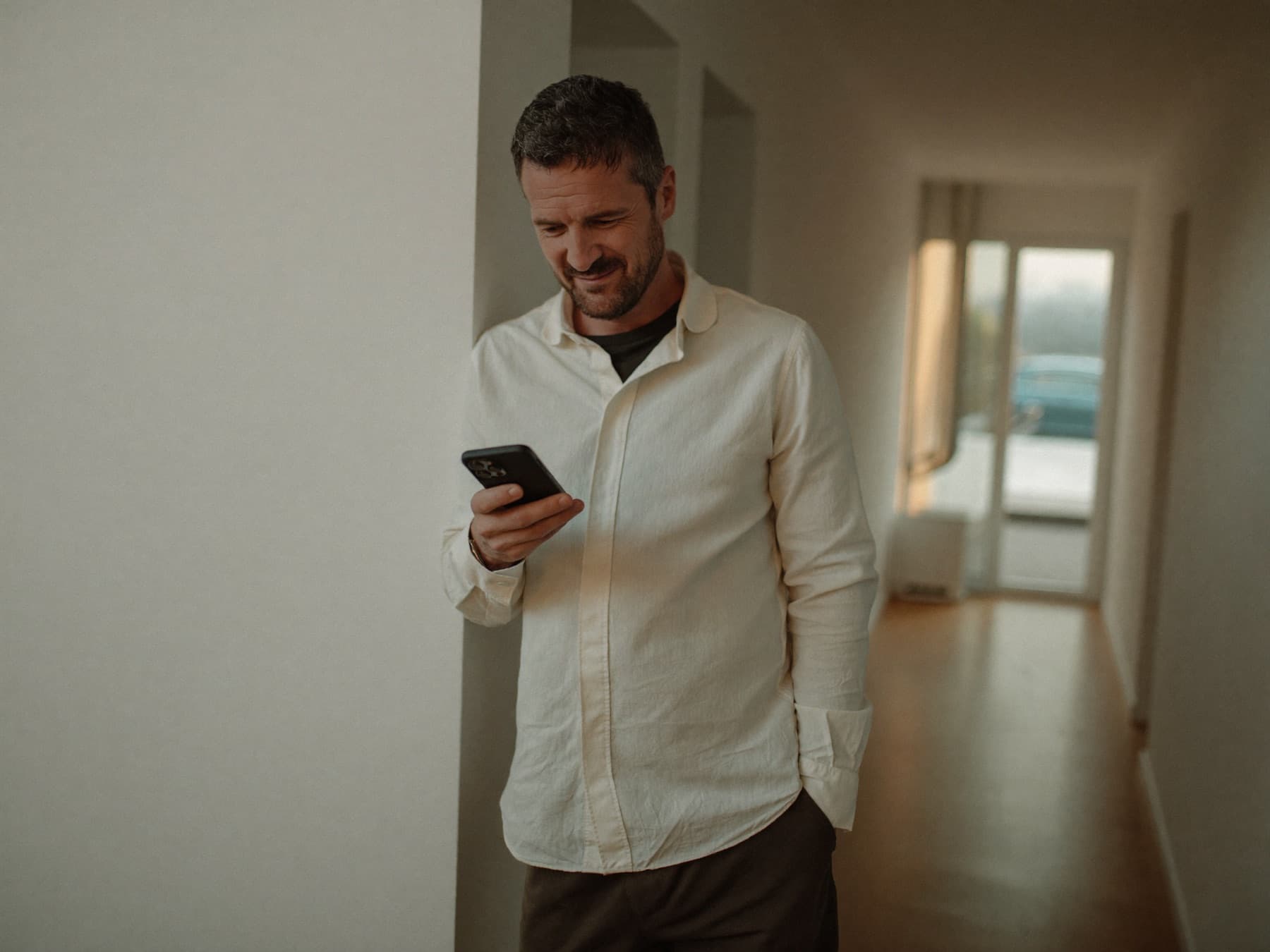 Man kijkt in de hal van zijn woning ontspannen op zijn telefoon.